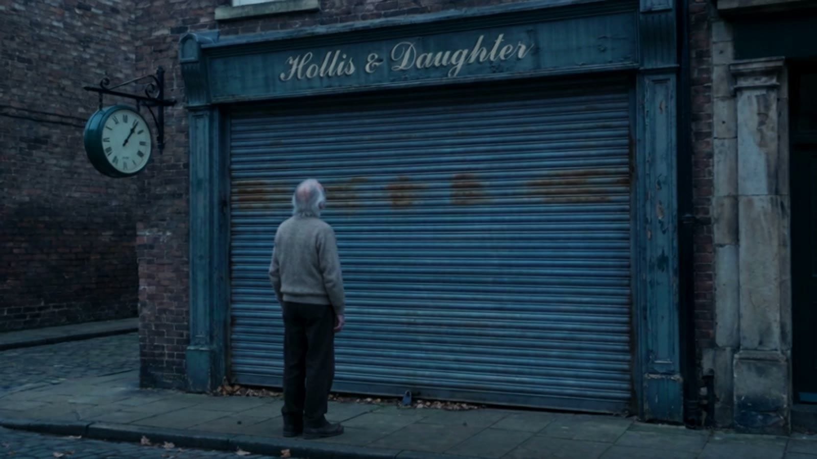 An old man stands before the shut blue shutter of Hollis & Daughter, a clock still hanging above the door
